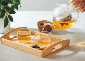 hand-pouring-tea-from-glass-teapot-wooden-serving-tray (1)