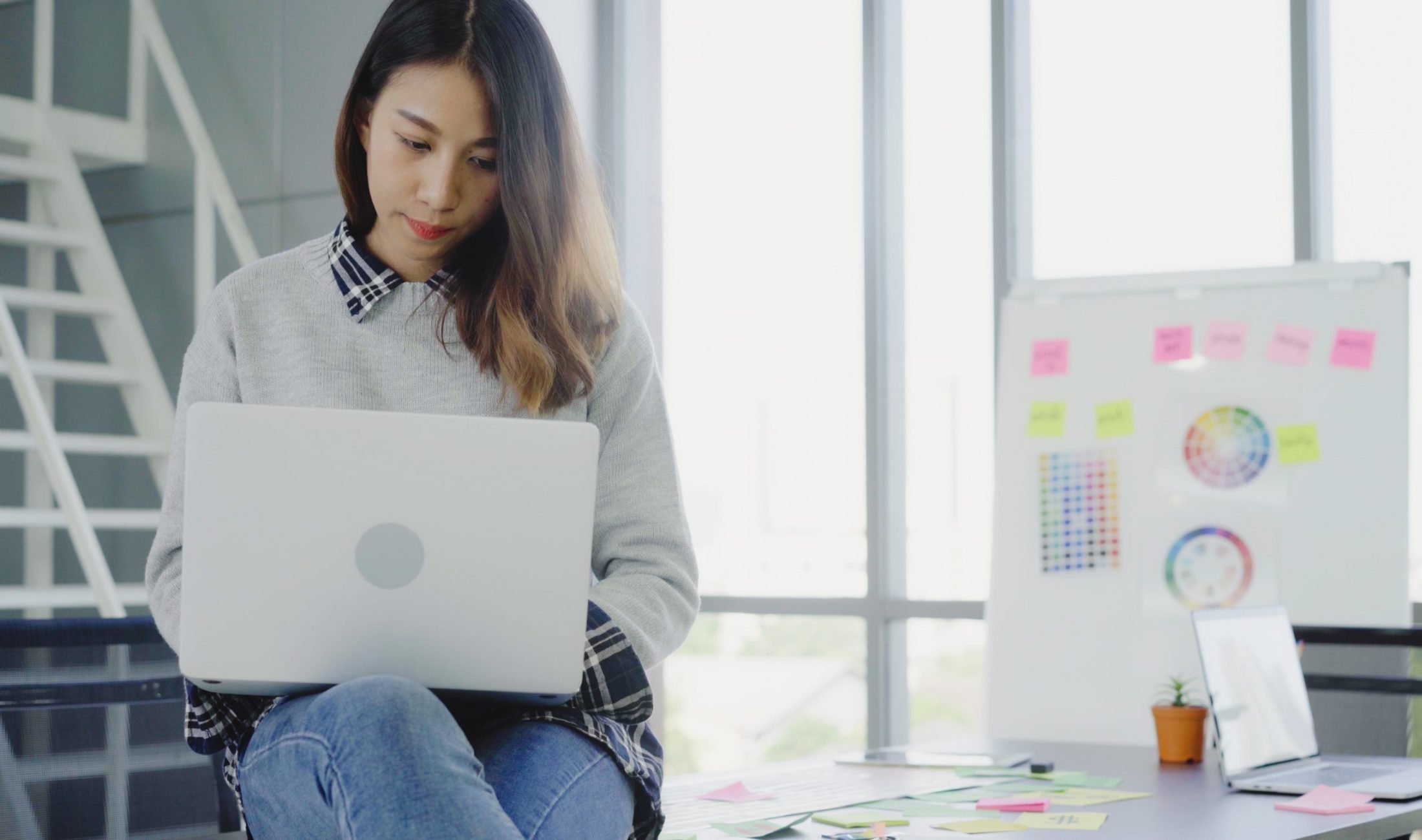 Professional Asian businesswoman working at her office via laptop. Young Asian female manager using portable computer device while sitting at modern workplace.
